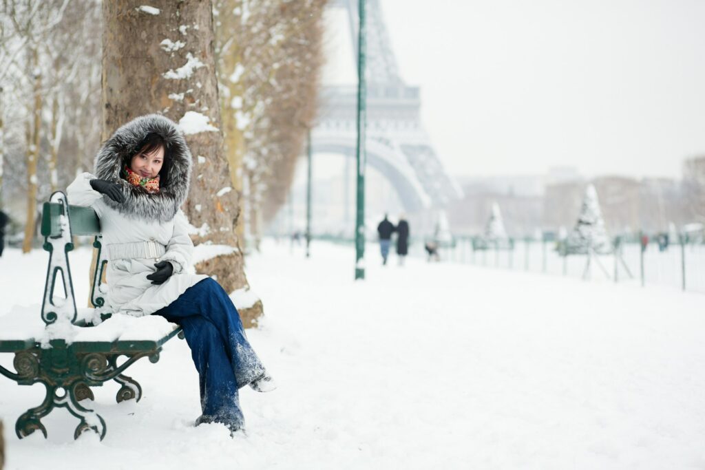Une dame sur un banc enneigé, près de la tour Eiffel.
