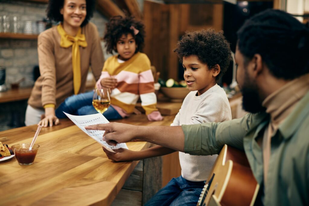 Des adultes révisent une partition de piano avec deux enfants dans une cuisine.