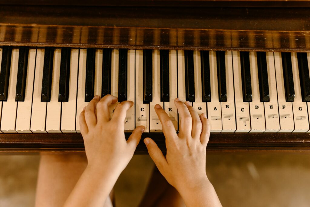 Des mains d'enfant sur un piano en train de jouer la note Do.