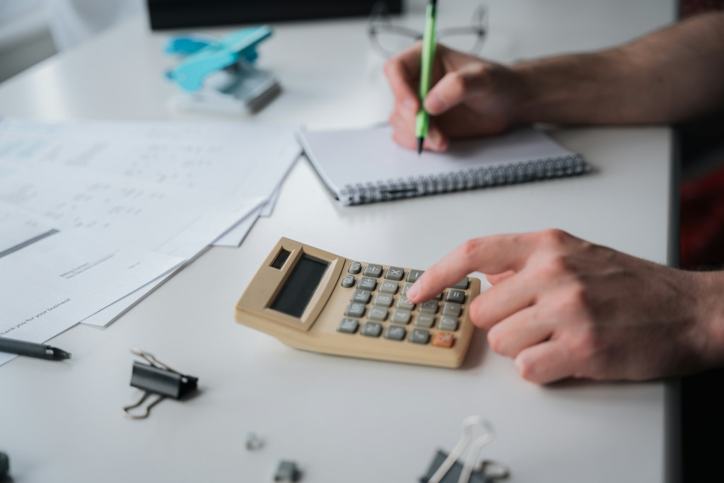 Une personne fait des calculs avec une calculatrice et un carnet de notes.