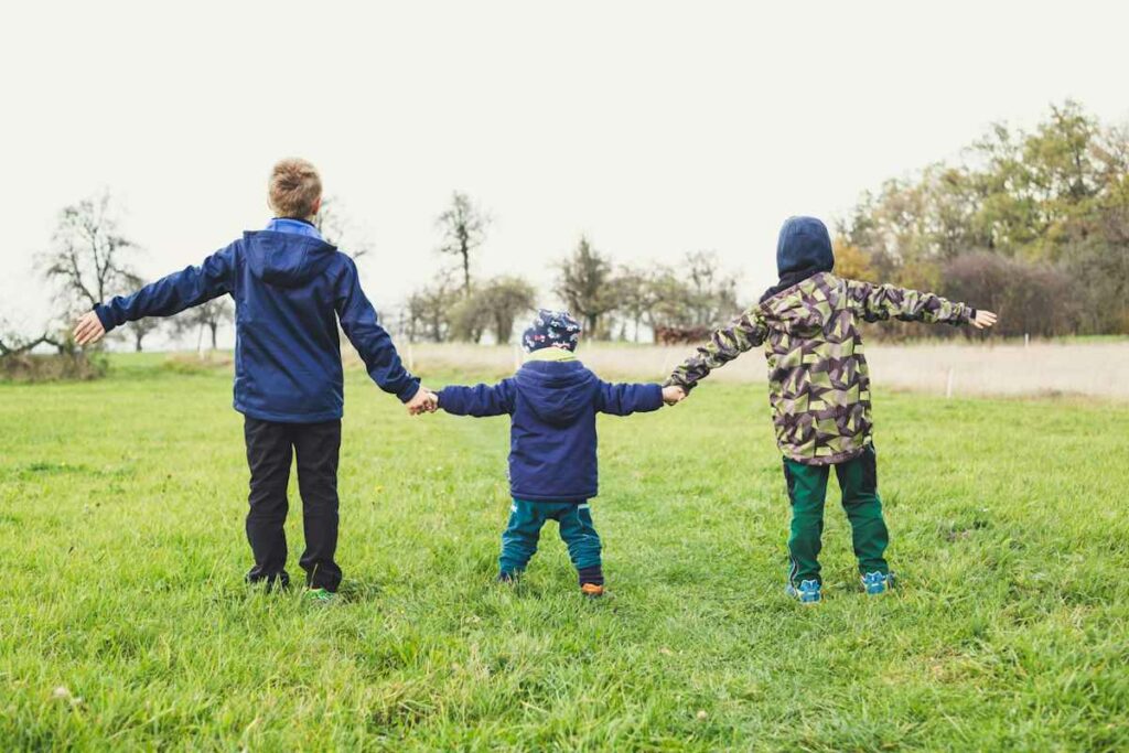 Des enfants se tiennent la main sur une pelouse verte, par un temps gris.