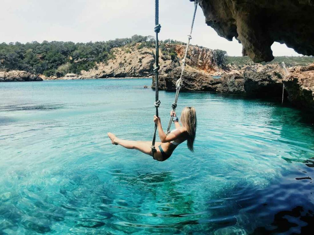 Une femme en maillot de bain se balance sur une corde au-dessus de l'eau turquoise.