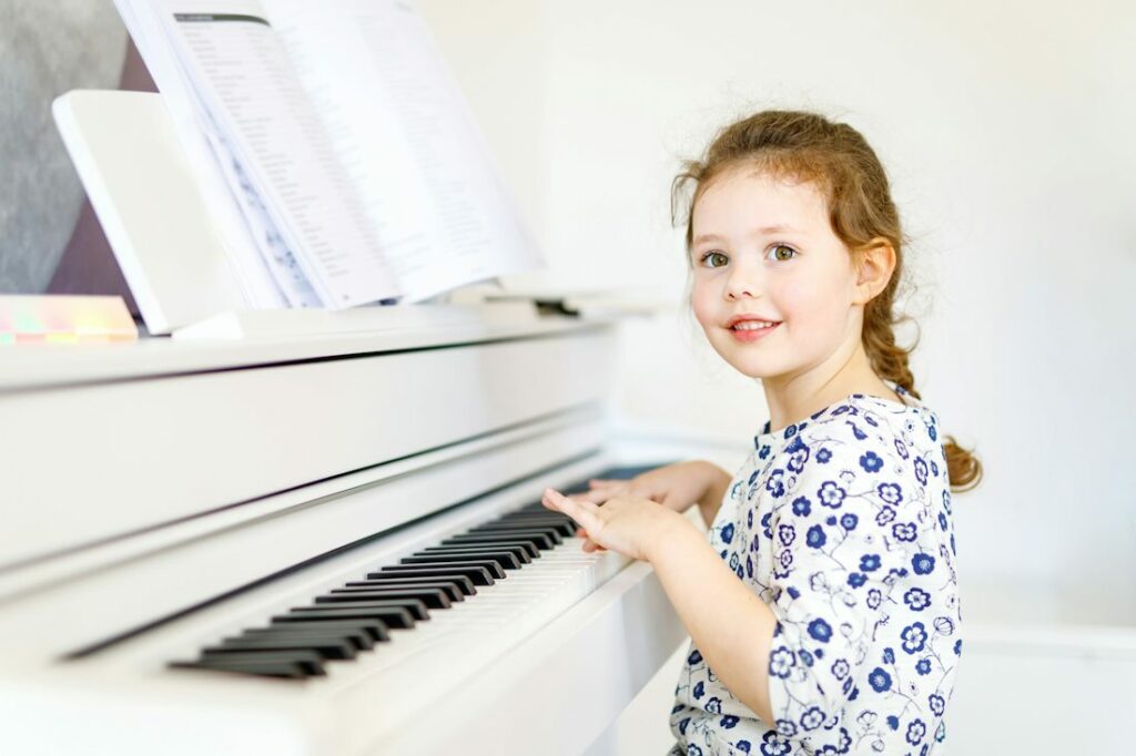 Une petite fille sourit sur un piano blanc.