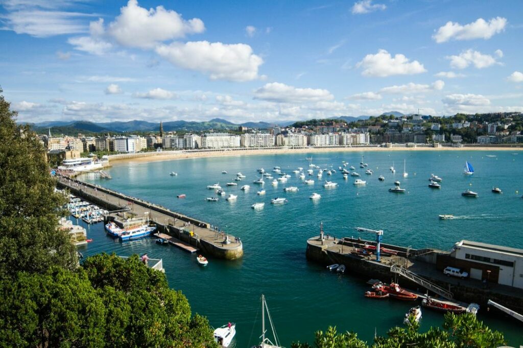 Vue d'une ville au bord de la mer, avec des bateaux et un massif montagneux.