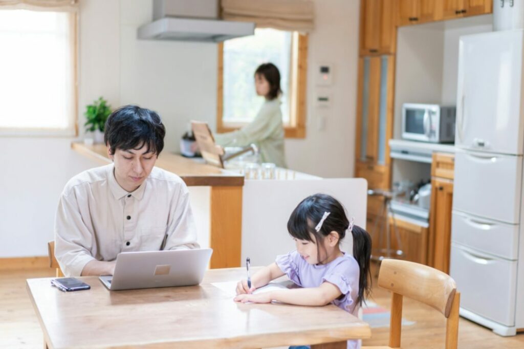 Un adulte travaille avec une petite fille à la maison, avec une femme au second plan.