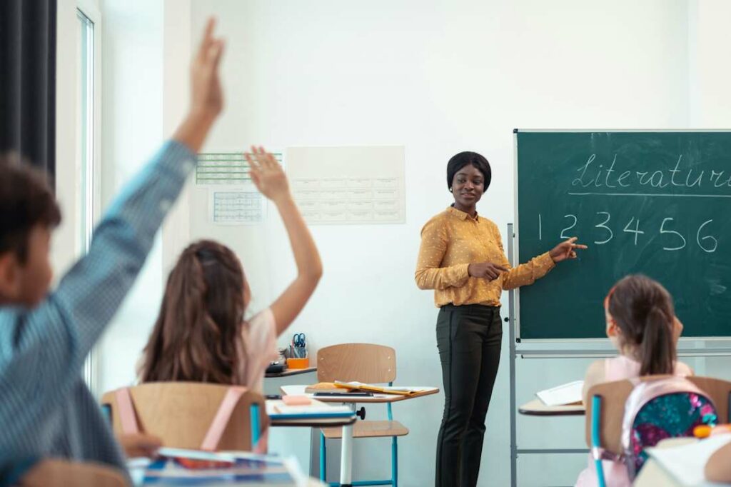 Une professeure se tient debout, devant ses élèves dans une salle lumineuse.