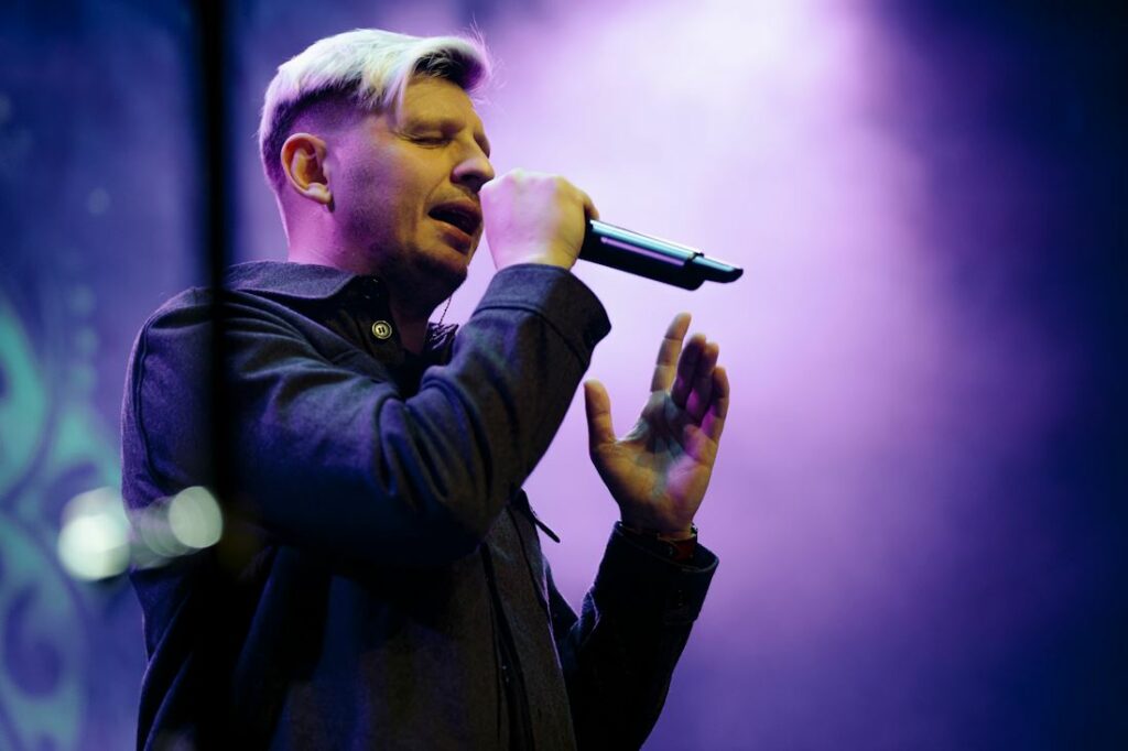 Vue d'un chanteur sur une scène avec une ambiance sombre de bleu et de violet.