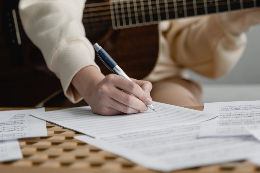 Une personne écrit de la musique sur une feuille avec une guitare entre les bras.