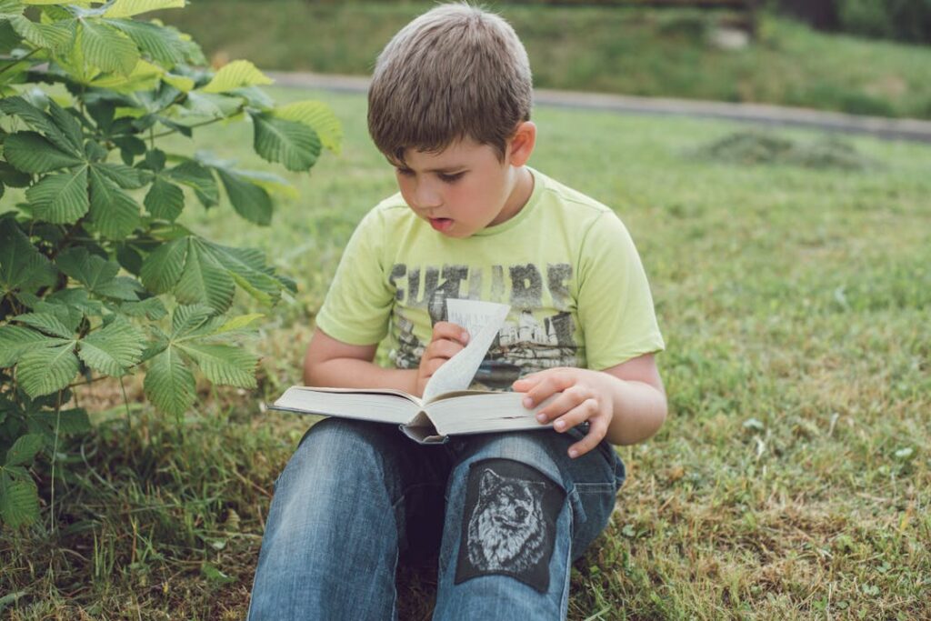 Un petit garçon en train de lire, assis dans l'herbe.