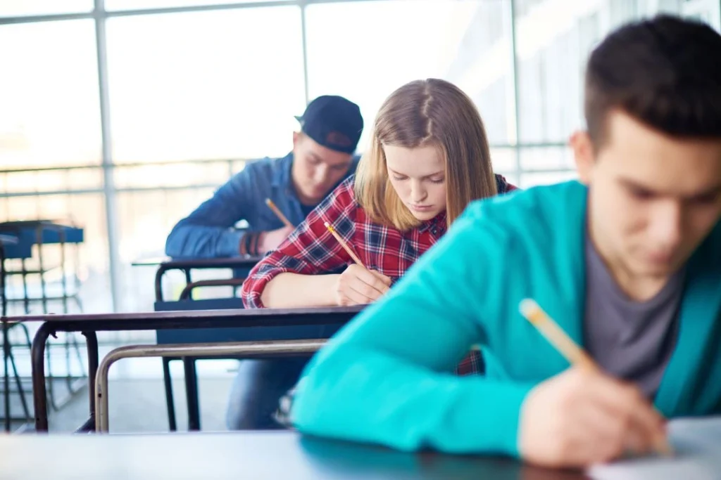 Trois élèves sont en train d'écrire sur une feuille lors d'un examen scolaire.