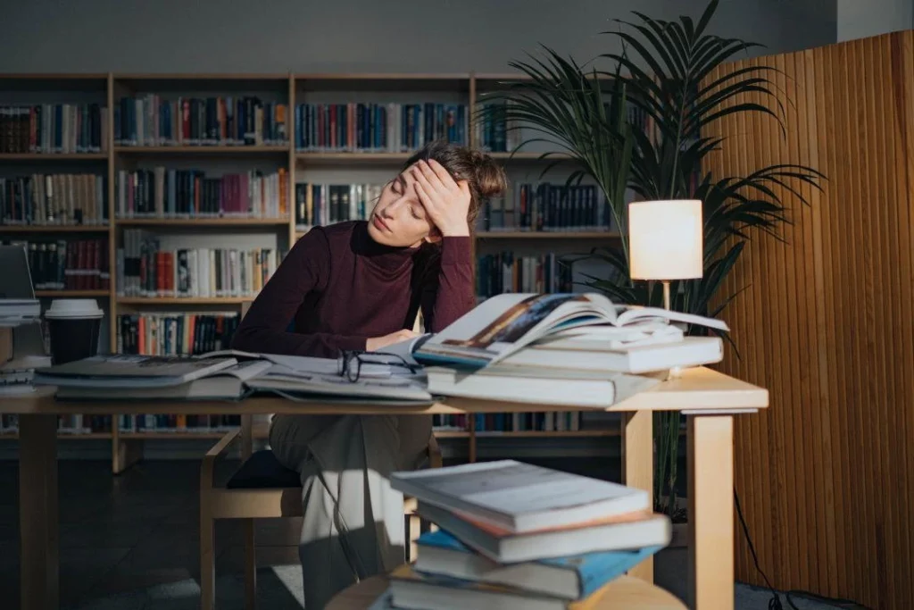 Une jeune étudiante semble exténuée par beaucoup de lecture sur un bureau.