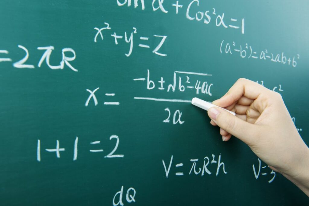 Vue d'un élève qui écrit un calcul mathématique avec une craie blanche.