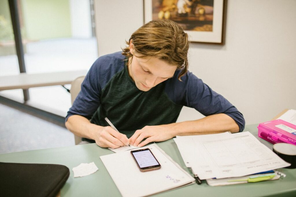 Un jeune homme est en train d'écrire des calculs sur une feuille avec une calculatrice.