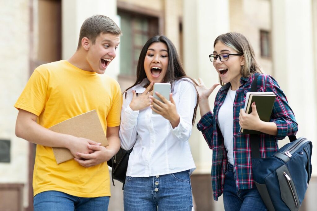 Trois étudiants semblent contents de ce qu'ils lisent sur un téléphone.