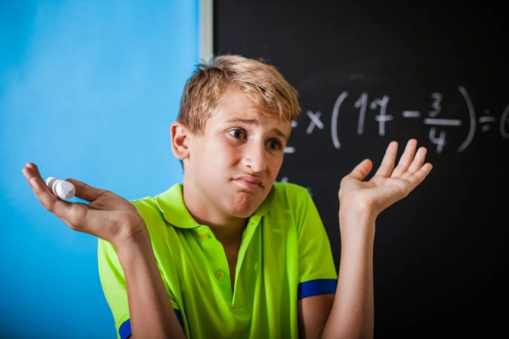 Un jeune élève semble ne pas savoir résoudre une opération mathématique devant un tableau noir.