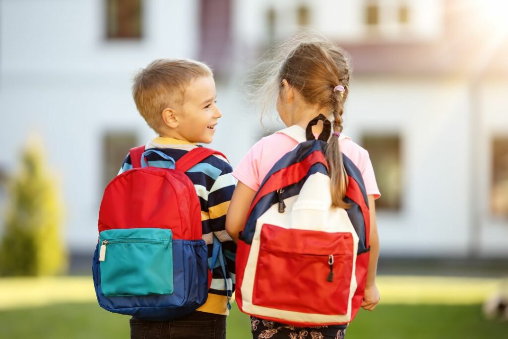 Deux élèves vus de dos, vont à l'école avec un cartable sur le dos.