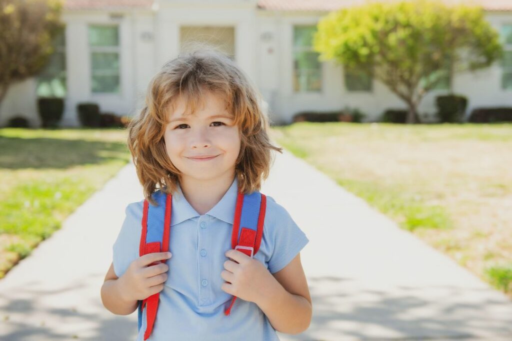 Un jeune garçon sourit avec un cartable sur le dos.