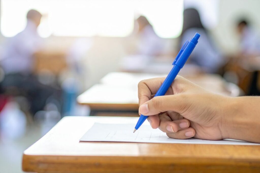 Main d'un élève rédigeant une épreuve écrite du bac de physique chimie dans une salle d'examen.