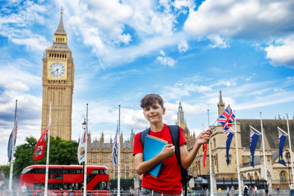 Jeune étudiant souriant devant Big Ben à Londres, tenant un cahier et un drapeau britannique.