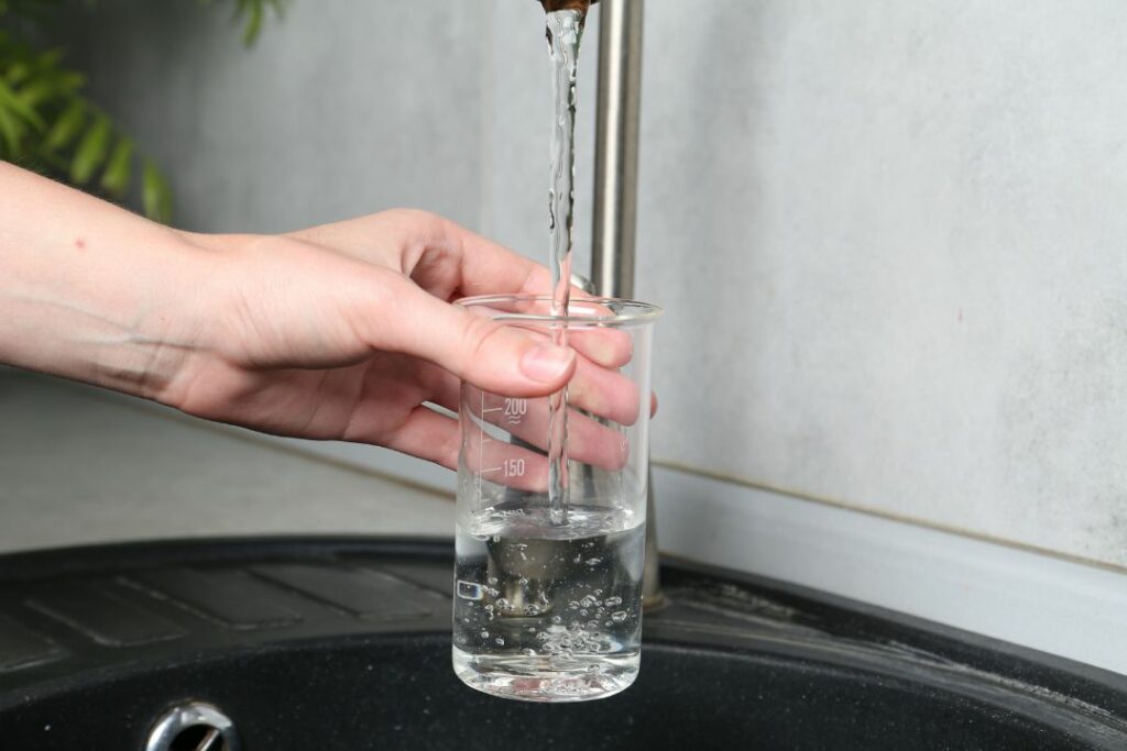 Main tenant un bécher gradué rempli d'eau sous un robinet lors d'une expérience de chimie.