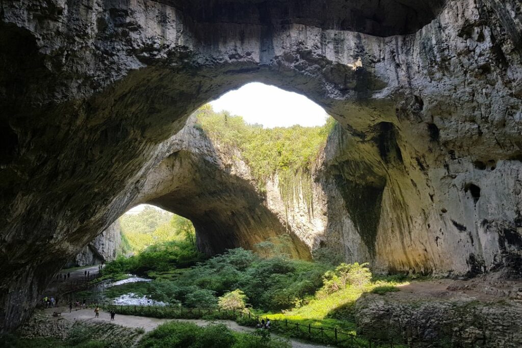 Une immense caverne ouverte sur la lumière du jour, évoquant l'allégorie de la caverne de Platon.