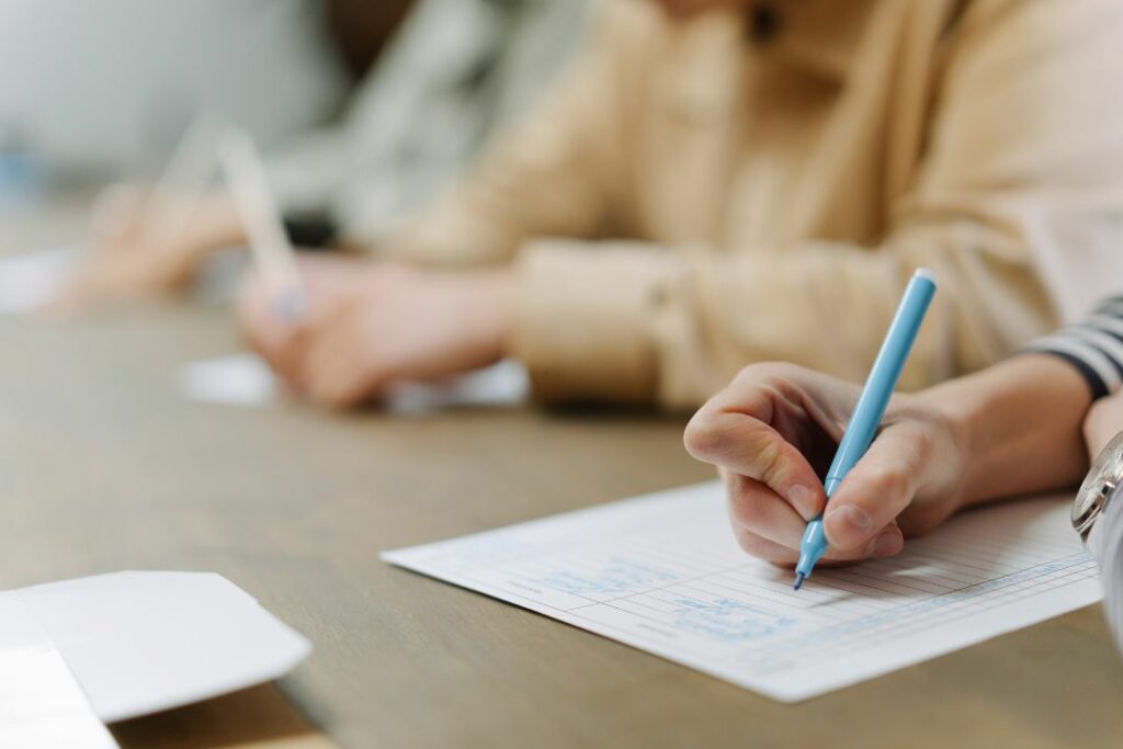 Une élève rédige sur sa copie en classe, stylo bleu à la main.