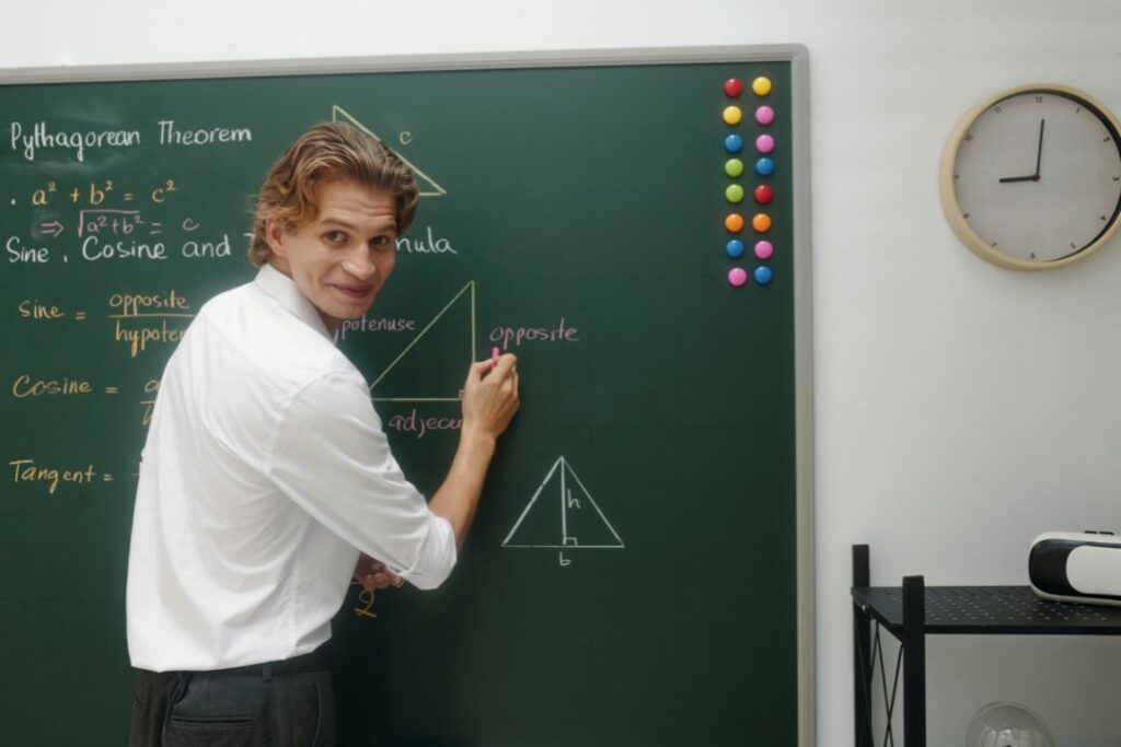 Un professeur se retourne en souriant pendant qu'il écrit des formules de géométrie au tableau.